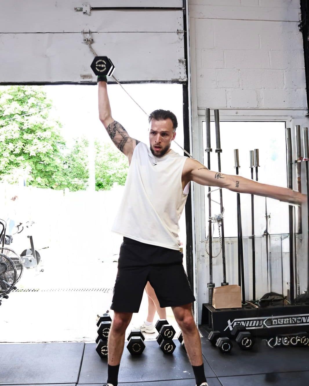 Un coach, haltère levé à bout de bras, en pleine séance dans une salle de sport.
