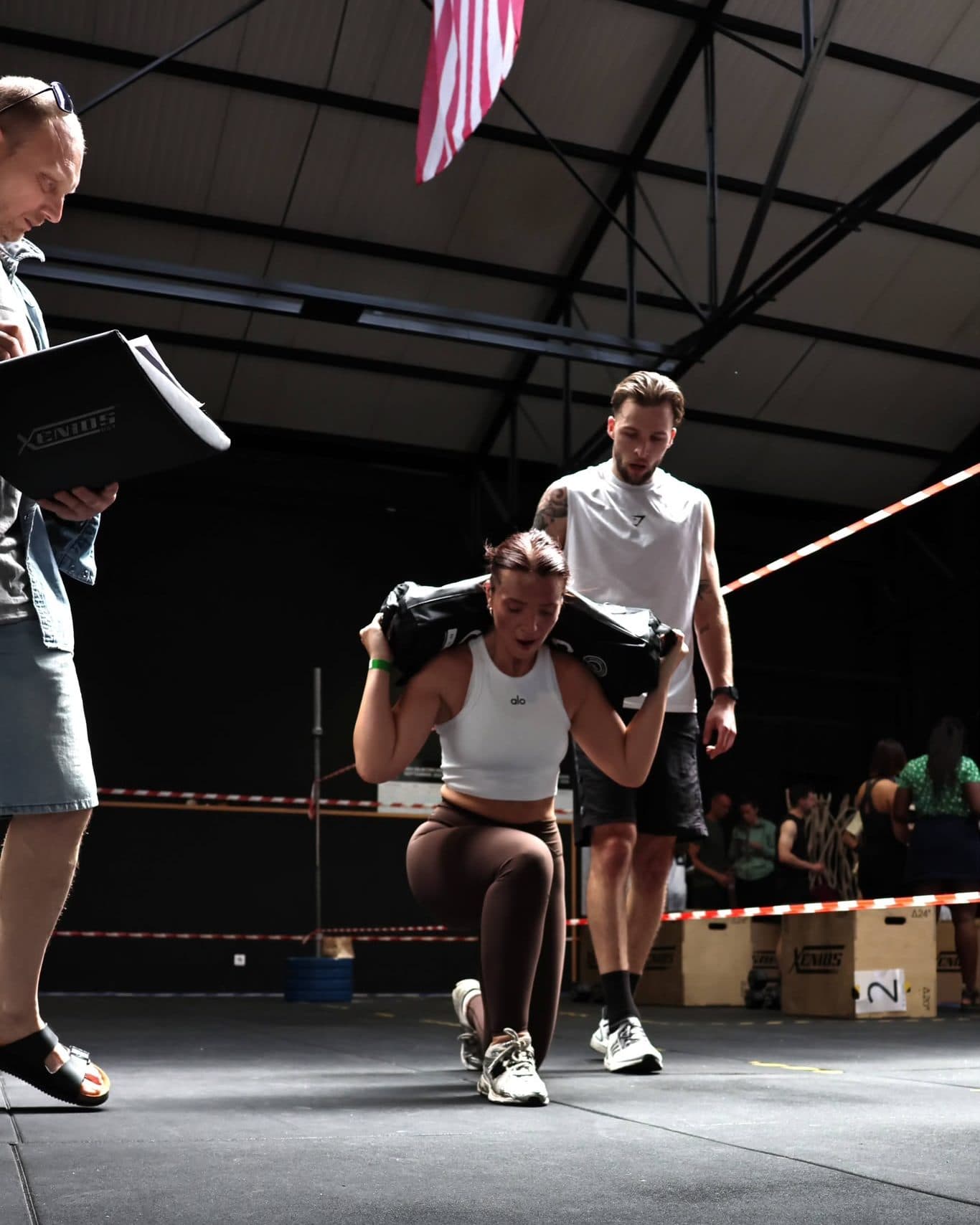 Une coachée porte un sac lesté en fente, un coach l'accompagne pendant l'effort.